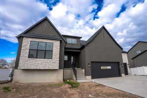 View of front facade with stone siding, concrete driveway, stucco siding, and an attached garage