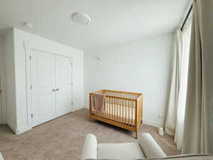 Bedroom featuring a nursery area, a closet, and light colored carpet