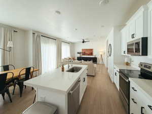 Kitchen with stainless steel appliances, a center island with sink, white cabinets, open floor plan, and dark wood finished floors