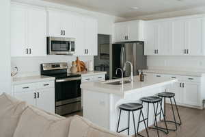 Kitchen featuring stainless steel appliances, a kitchen island with sink, a kitchen bar, white cabinets, and dark wood finished floors