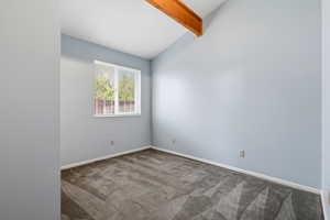 Empty room with carpet floors and vaulted ceiling with beams