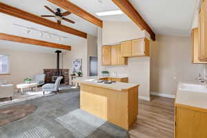 Kitchen with light countertops, open floor plan, a wood stove, light wood finish cabinets, and vaulted ceiling