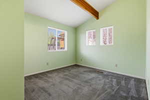 Spare room featuring lofted ceiling with beams and dark carpet