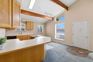 Kitchen featuring light countertops, lofted ceiling with beams, a peninsula, light colored carpet, and black dishwasher