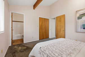 Bedroom featuring dark carpet, connected bathroom, and vaulted ceiling with beams