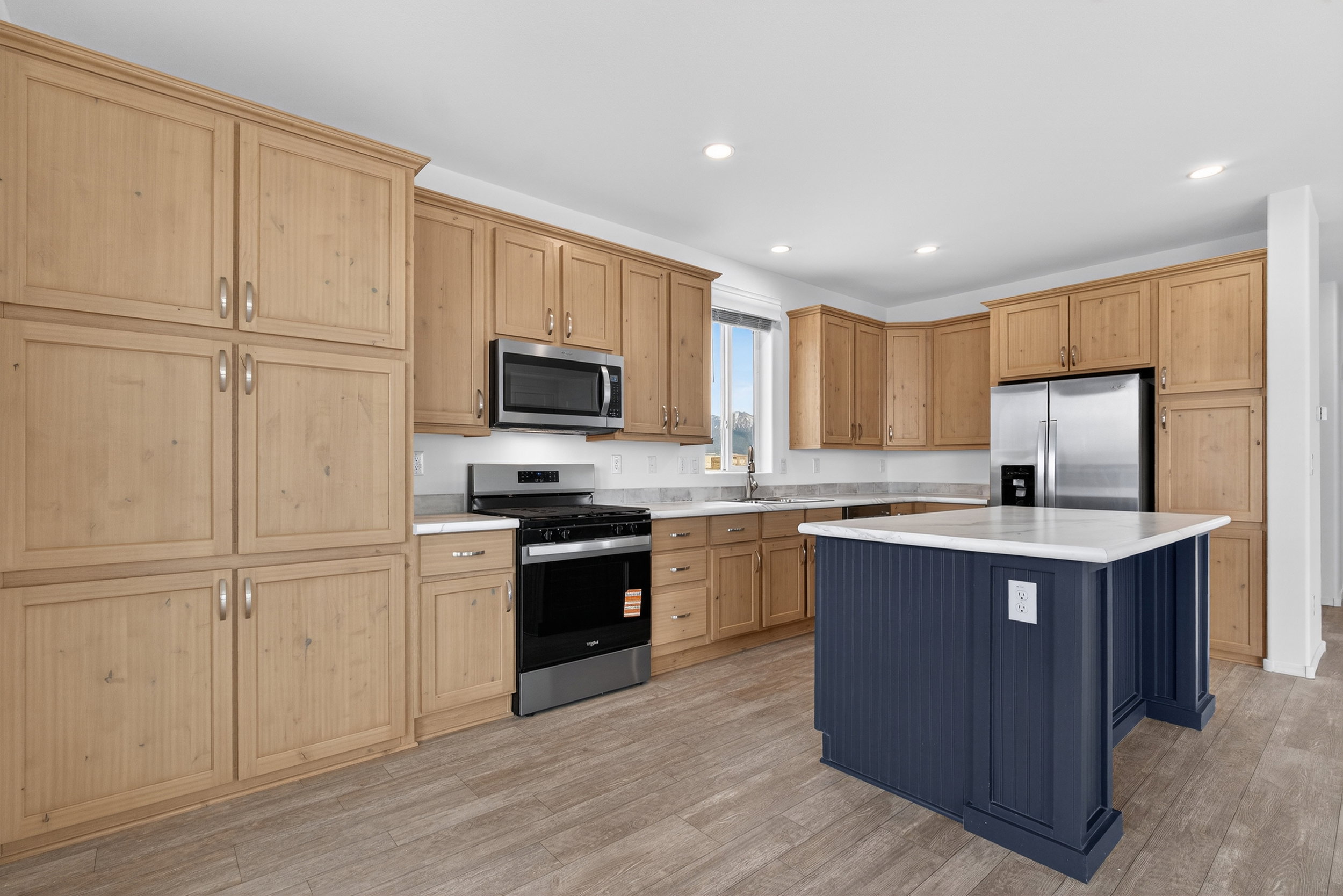 Kitchen with stainless steel appliances, light wood-type flooring, a center island, dual tone cabinetry, and recessed lighting