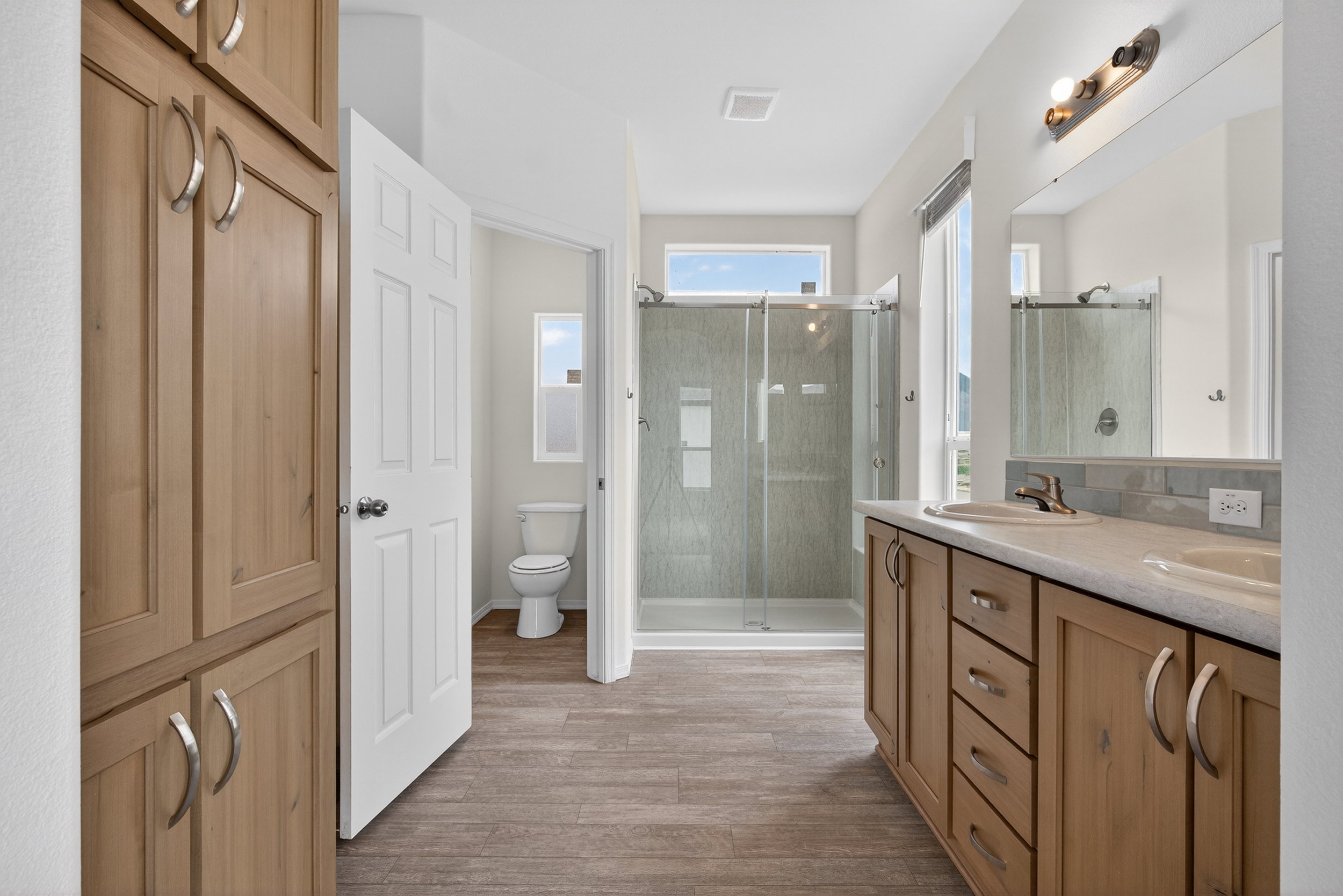 Bathroom featuring double vanity, light wood-style floors, and a shower stall