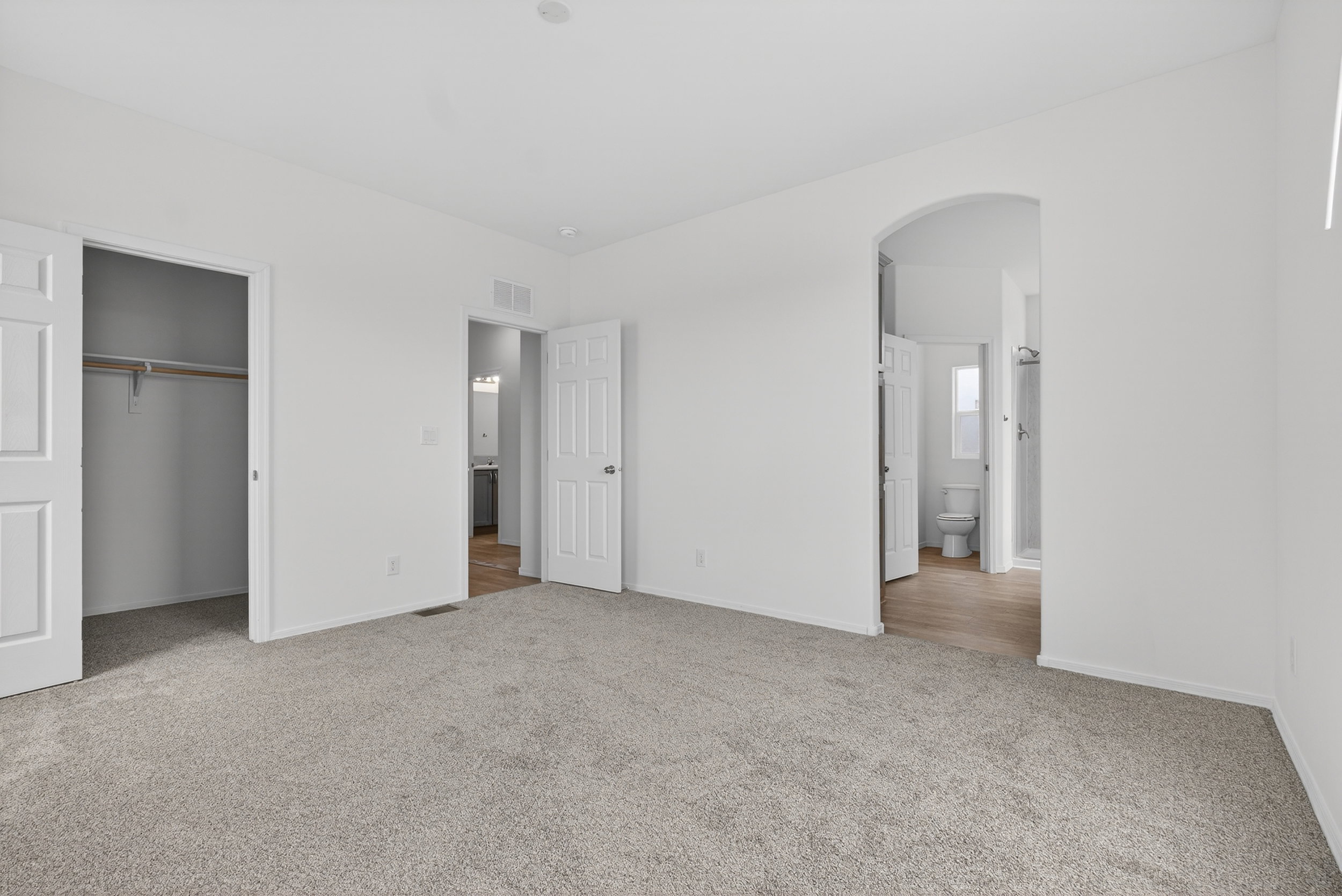 Unfurnished bedroom featuring arched walkways, light carpet, and a spacious closet