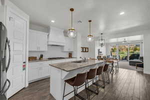 Kitchen with light stone counters, stainless steel appliances, a breakfast bar area, a kitchen island with sink, and dark wood-style flooring