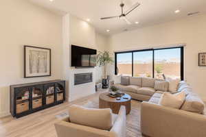 Living room with a ceiling fan, light wood finished floors, a glass covered fireplace, recessed lighting, and a high ceiling