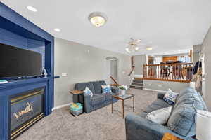 Living area with arched walkways, carpet flooring, recessed lighting, ceiling fan, and a large fireplace