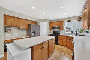 Kitchen with a center island, stainless steel appliances, light countertops, stone tile flooring, and recessed lighting