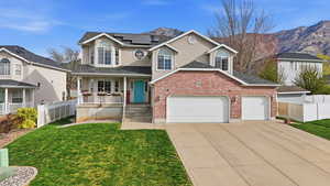 Traditional-style house with a garage, covered porch, solar panels, driveway, and brick siding