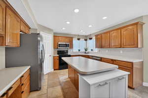 Kitchen with stainless steel appliances, light countertops, wood finish cabinetry, a kitchen island, and recessed lighting