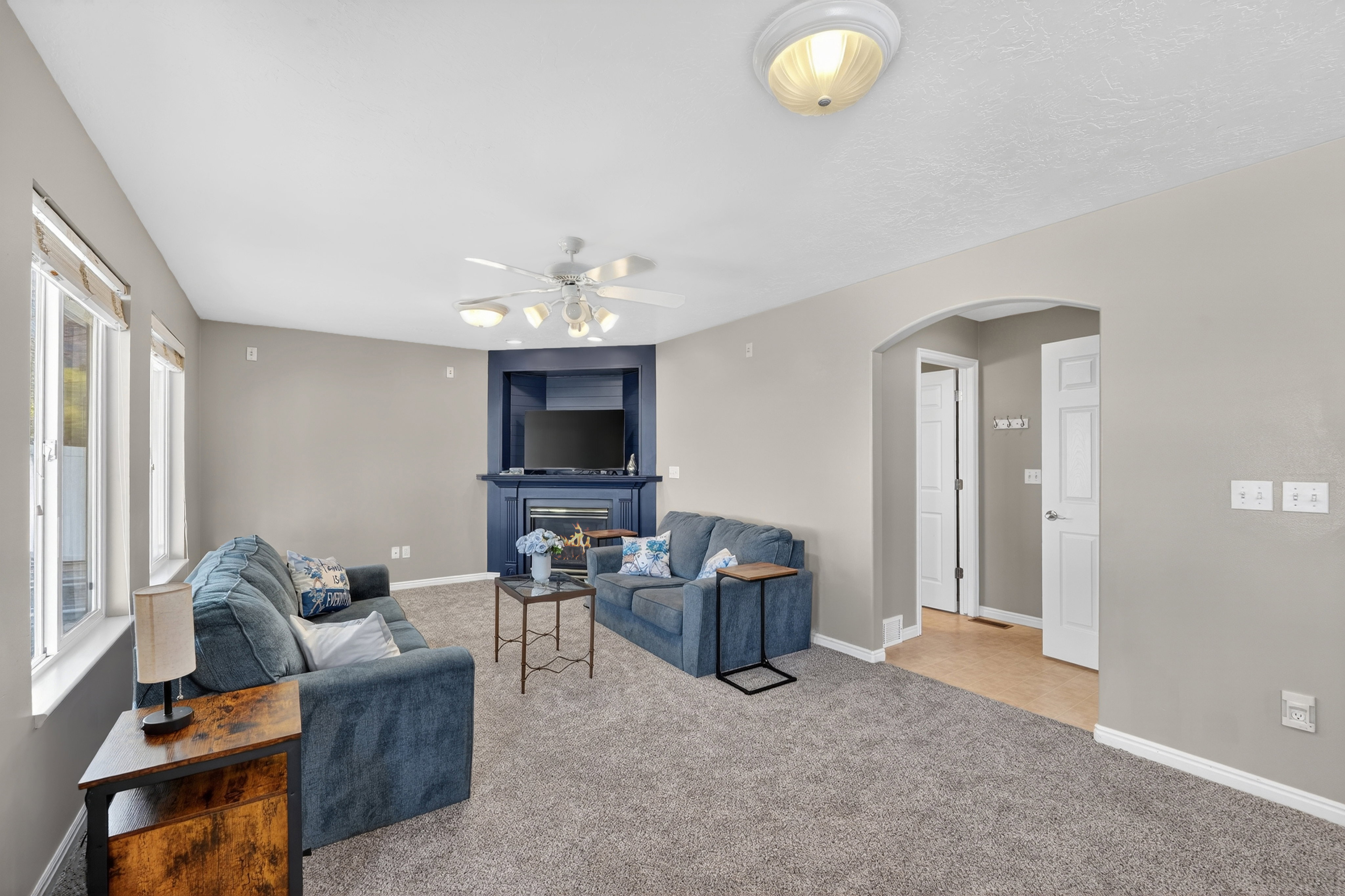 Living area featuring arched walkways, a ceiling fan, light colored carpet, and a glass covered fireplace