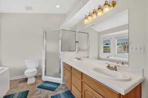 Full bath featuring a garden tub, double vanity, a stall shower, vaulted ceiling, and light stone finish flooring