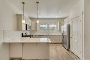 Kitchen featuring a peninsula, a kitchen bar, stainless steel appliances, pendant lighting, and light wood-style floors