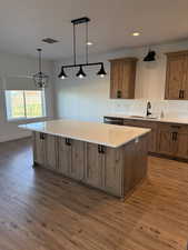 Kitchen featuring dark wood finished floors, pendant lighting, a large island, dishwasher, and wood finish cabinets