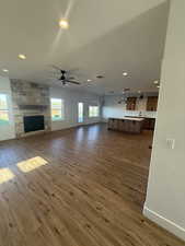 Unfurnished living room with a stone fireplace, recessed lighting, dark wood-type flooring, and a ceiling fan