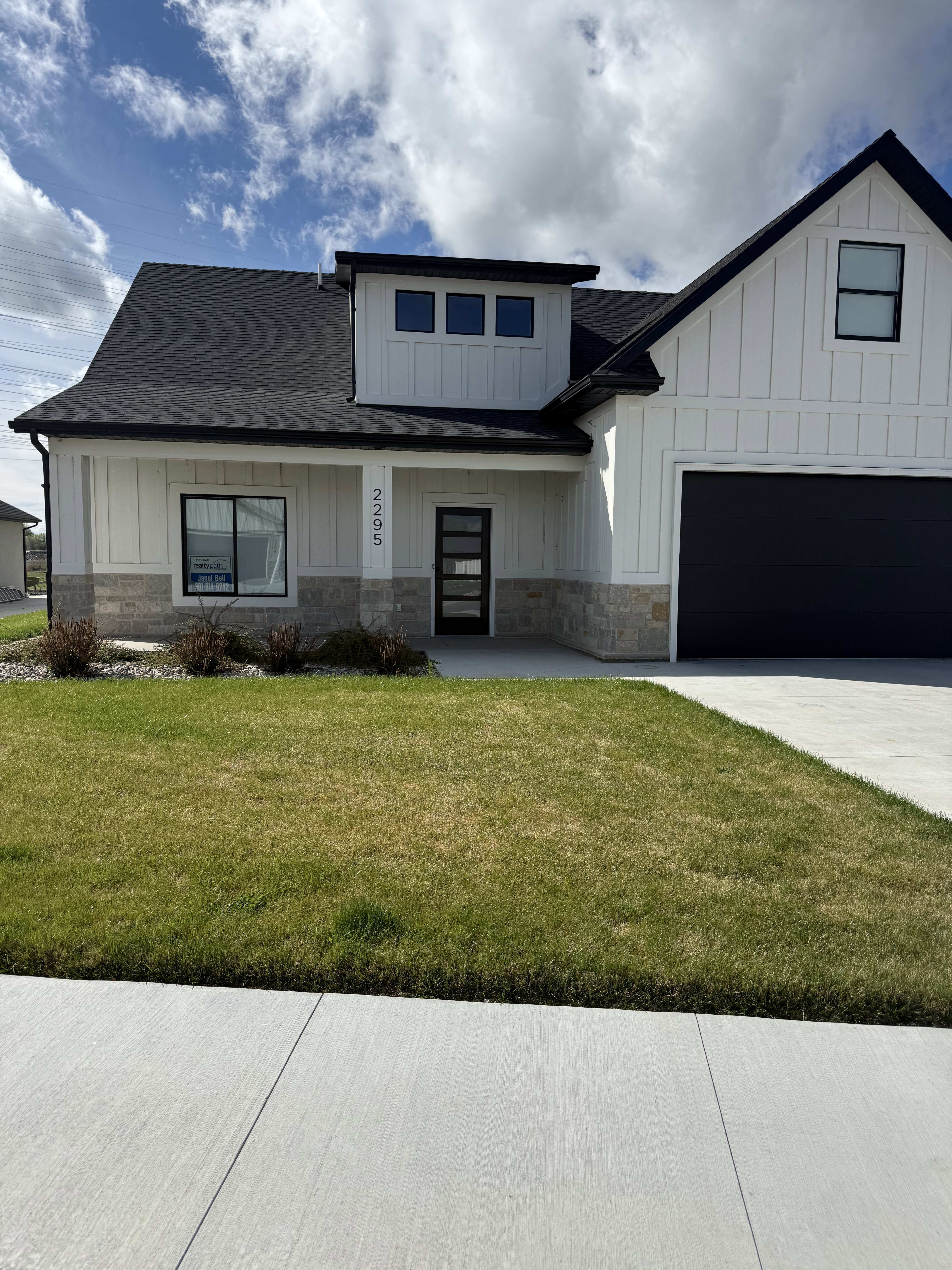 Modern inspired farmhouse with board and batten siding, a front yard, stone siding, and roof with shingles