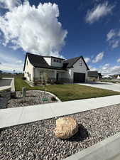 Modern farmhouse with board and batten siding, driveway, stone siding, a shingled roof, and a front lawn