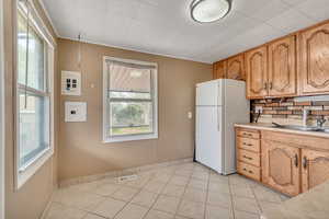 Kitchen featuring light countertops, freestanding refrigerator, decorative backsplash, and light tile patterned flooring