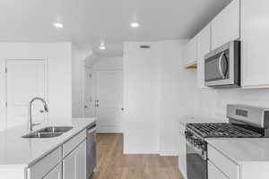 Kitchen with stainless steel appliances, light wood-style floors, white cabinetry, light stone countertops, and recessed lighting