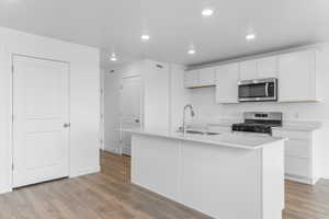 Kitchen with a center island with sink, stainless steel appliances, white cabinets, light wood-type flooring, and recessed lighting