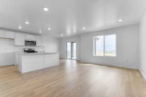 Kitchen with white cabinets, open floor plan, a kitchen island with sink, light wood-style flooring, and recessed lighting