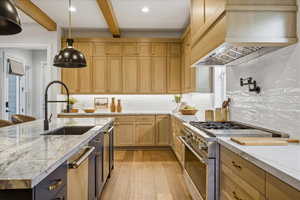 Kitchen with stainless steel appliances, light wood finished floors, beamed ceiling, an island with sink, and decorative backsplash