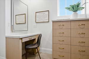 Primary walk in closet featuring light colored carpet, built in dresser, vanity, one of two closets in primary