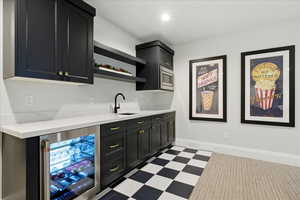 Bar area with dark cabinets, beverage cooler, light floors, open shelves, and light stone counters, monogram mini fridge