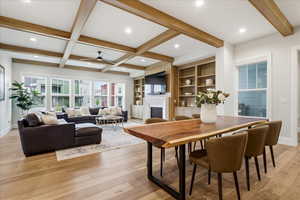Dining room with beam ceiling, a fireplace, ceiling fan, light wood flooring, and built in shelves