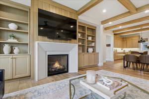 Living room with built in features, beamed ceiling, light wood flooring, recessed lighting, and a lit fireplace