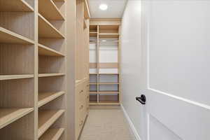 Primary walk in closet featuring light colored carpet, built in dresser, one of two closets in primary