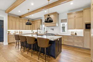 Kitchen with tasteful backsplash, light wood-type flooring, a breakfast bar, a center island with sink, and light stone countertops