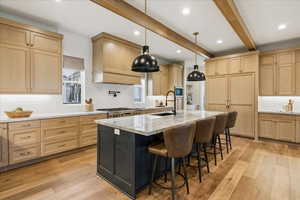 Two tone kitchen featuring decorative backsplash, light stone countertops, a kitchen island with sink, a kitchen bar, and dual tone cabinets