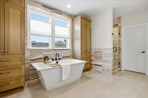 Primary Bathroom with tile walls, a shower stall, a soaking tub, and light tile patterned flooring, large storage cabinets