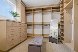 Primary walk in closet featuring light colored carpet, built in dresser, one of two closets in primary