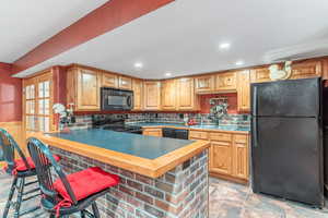 Kitchen with a kitchen bar, black appliances, decorative backsplash, a peninsula, and a wainscoted wall