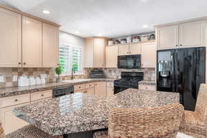 Kitchen with black appliances, light wood finish cabinets, a kitchen bar, recessed lighting, and tasteful backsplash