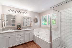 Bathroom featuring double vanity, a stall shower, a jetted tub, light wood-type flooring, and recessed lighting