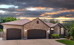 French country inspired facade with an attached garage, driveway, and brick siding