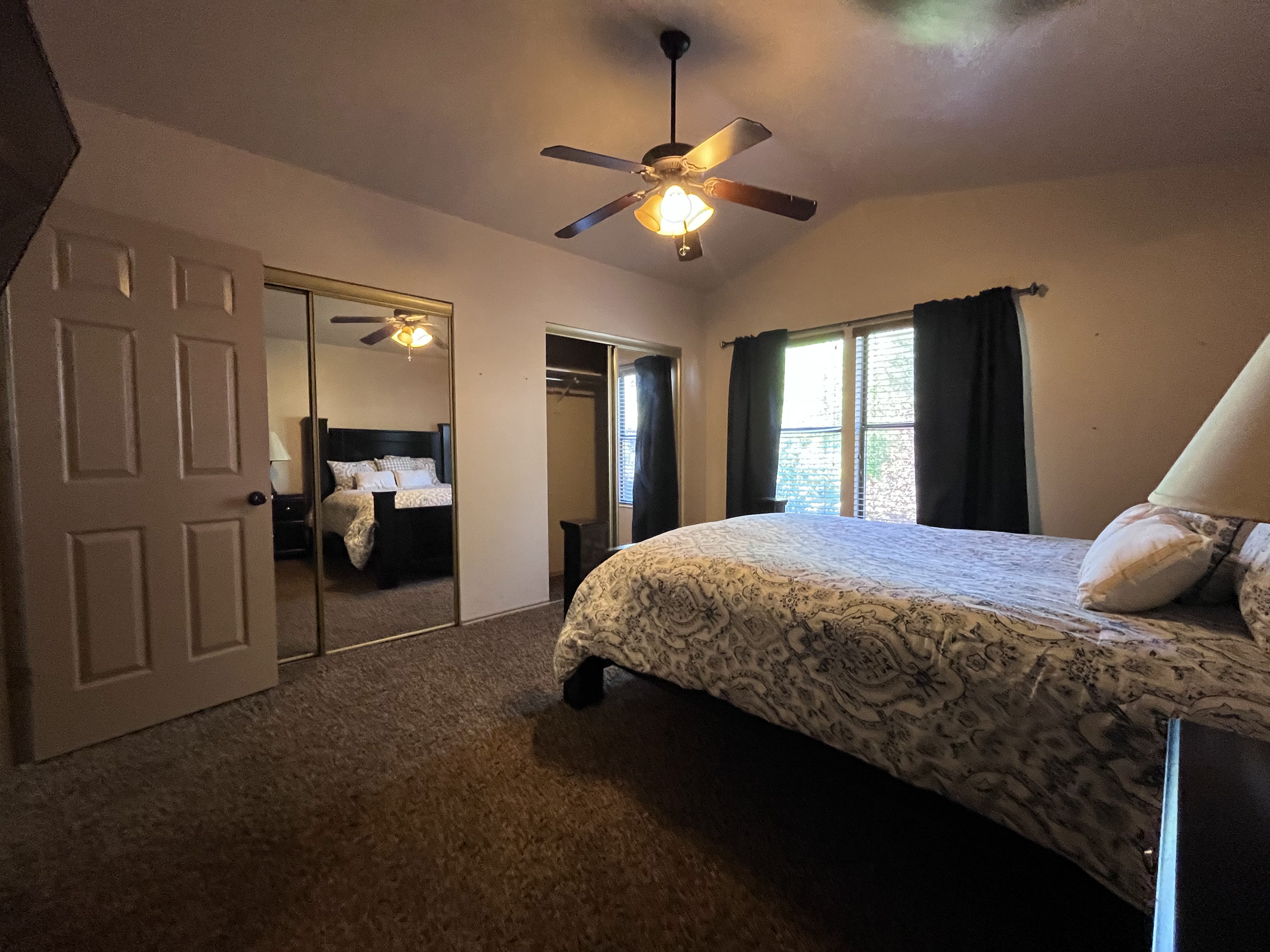 Bedroom featuring two closets, vaulted ceiling, dark carpet, and a ceiling fan