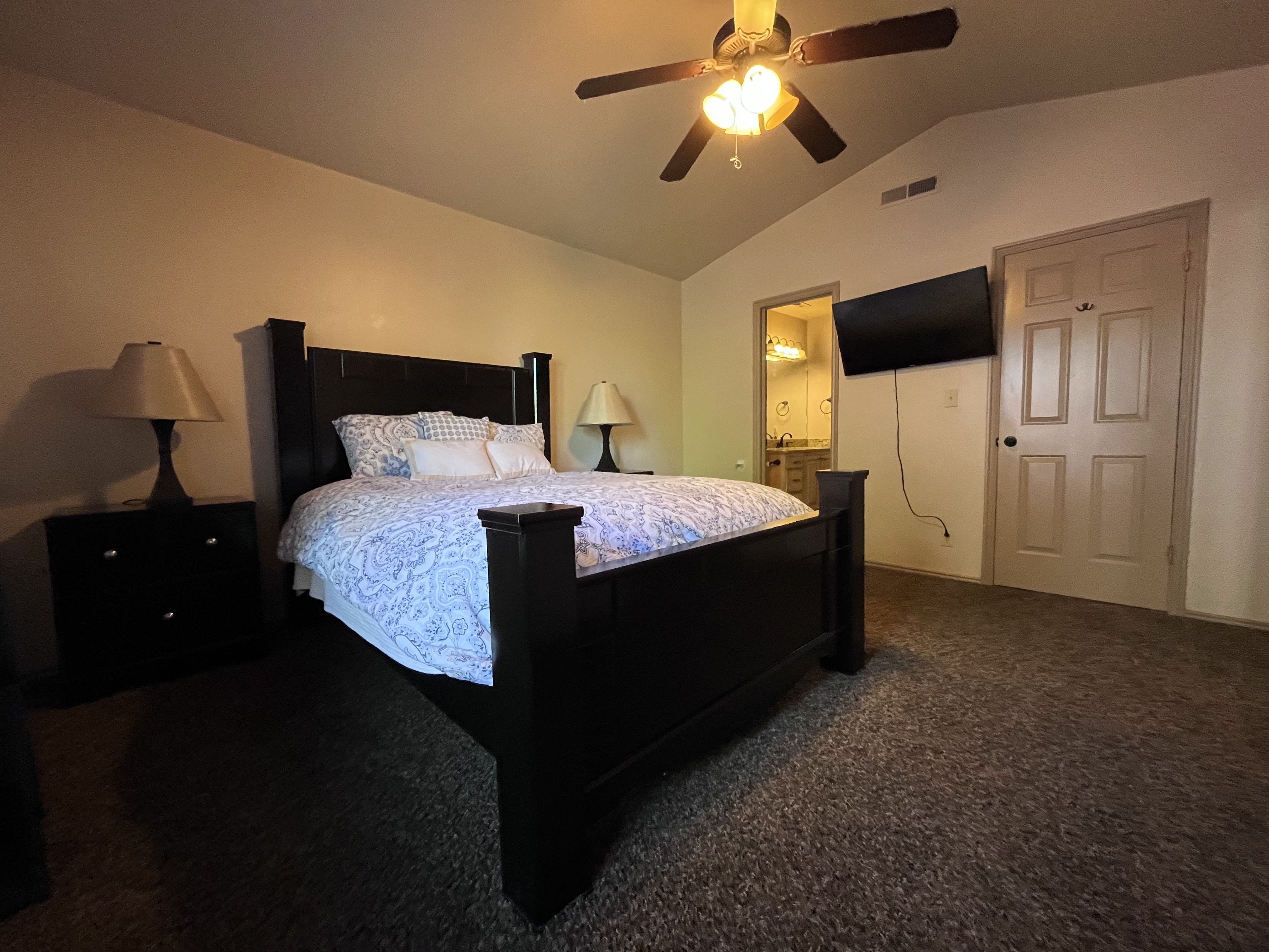 Bedroom with dark colored carpet, ceiling fan, and connected bathroom
