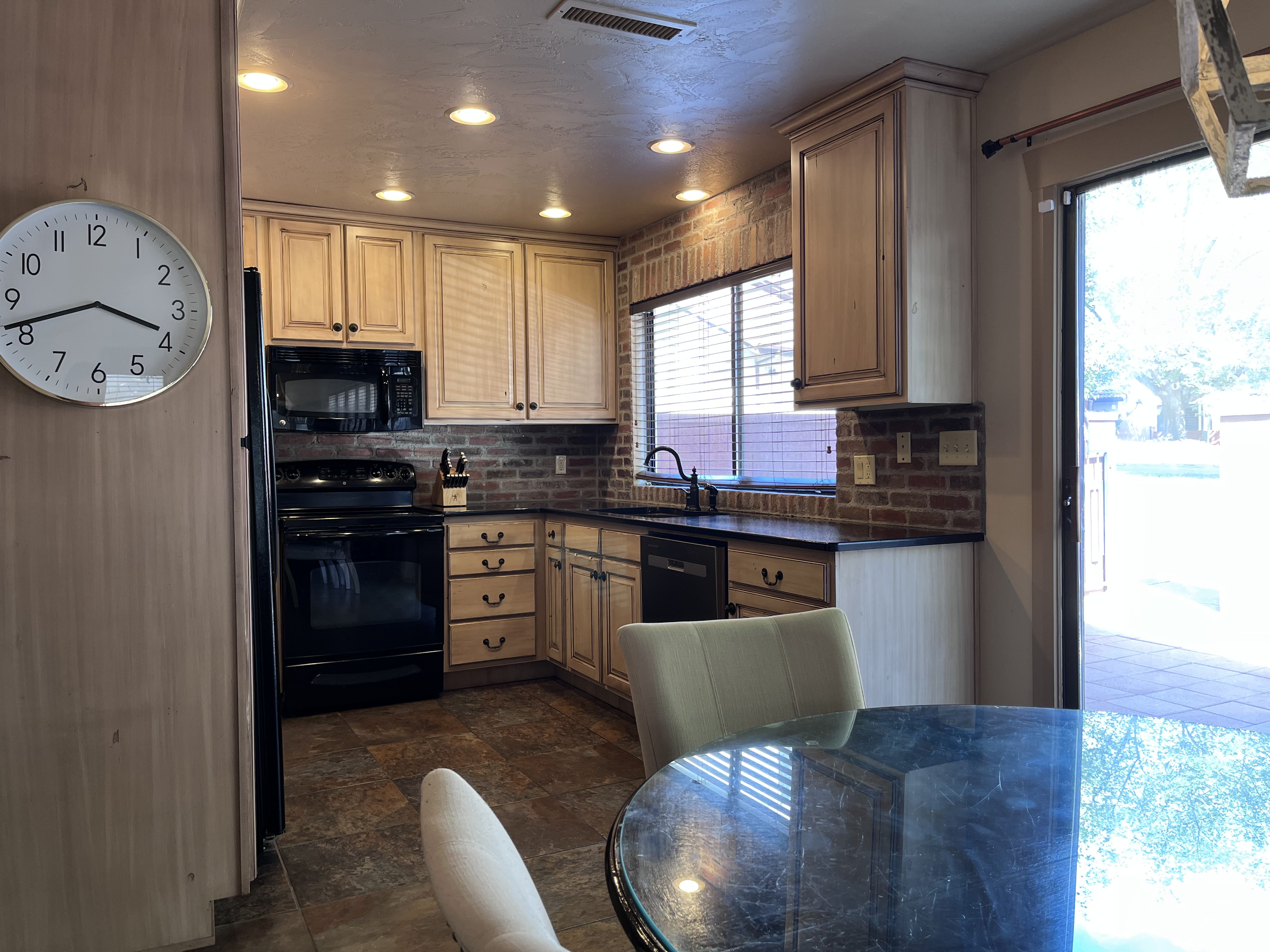 Kitchen featuring dark countertops, black appliances, tasteful backsplash, stone finish floors, and recessed lighting