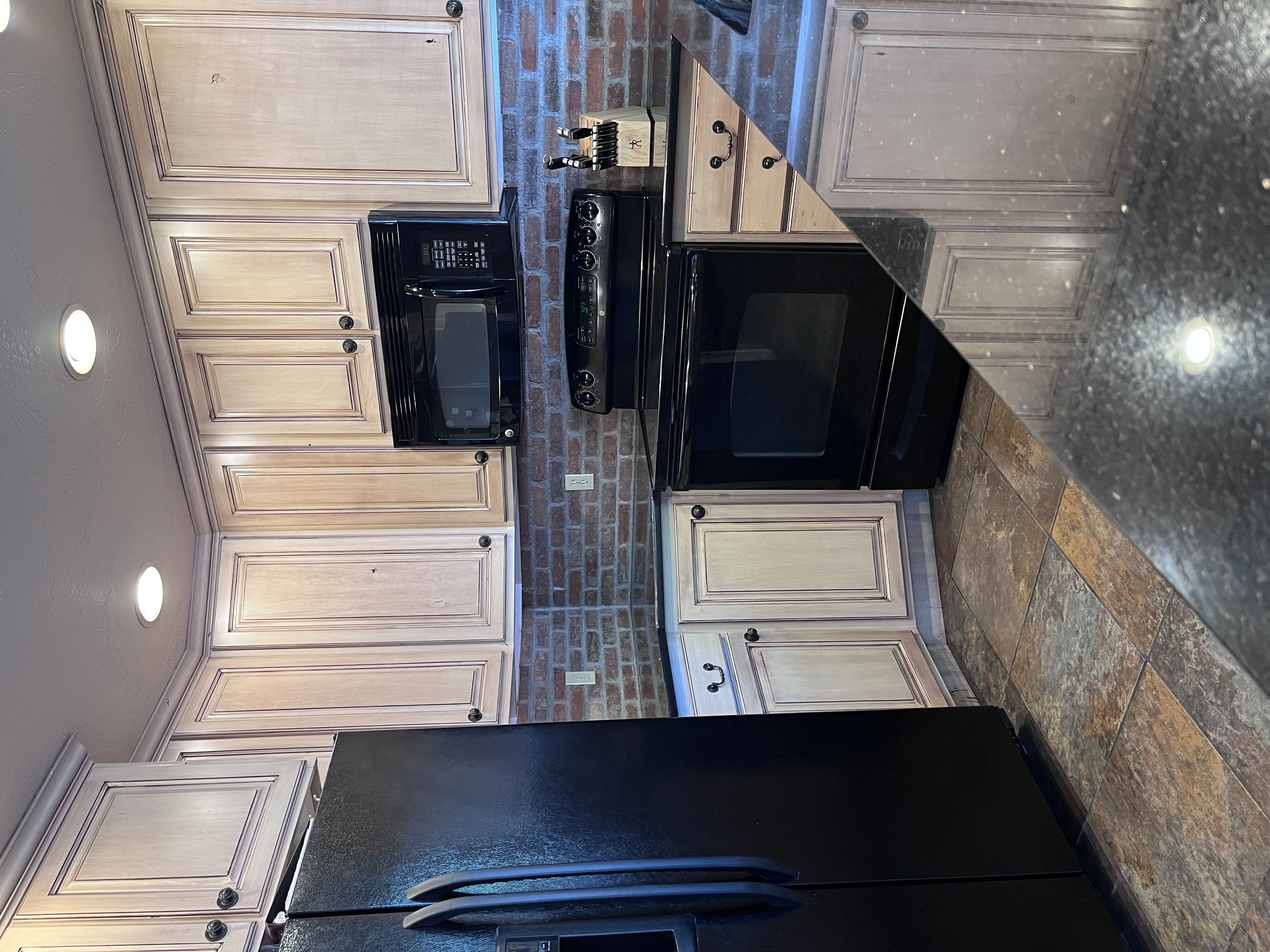Kitchen with black appliances, recessed lighting, backsplash, dark stone counters, and stone tile flooring