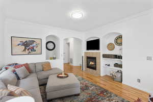 Living room featuring built in features, a fireplace, light wood-type flooring, ornamental molding, and arched walkways