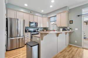 Kitchen with stainless steel appliances, a breakfast bar, a peninsula, light wood-type flooring, and recessed lighting
