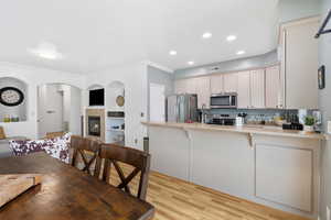 Kitchen featuring a peninsula, a tile fireplace, light wood-style flooring, built in shelves, and stainless steel appliances